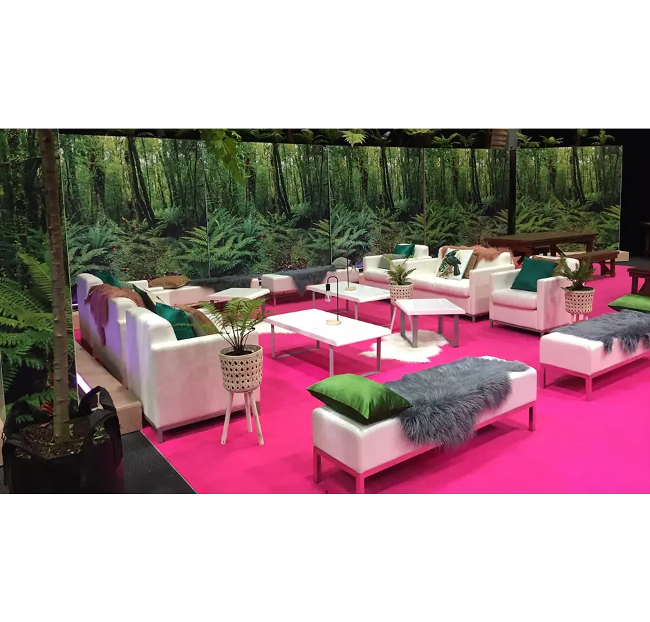 Peek Exhibition Lounge set up, images of forest printed on wall panels, bright pink carpet with white furniture and colorful throws